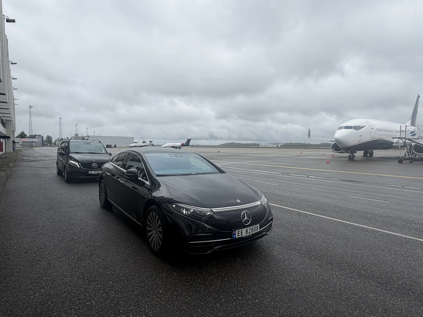 Svart Mercedes EQS fra Husby VIP på tarmac ved Oslo Lufthavn Gardermoen, med fly i bakgrunnen