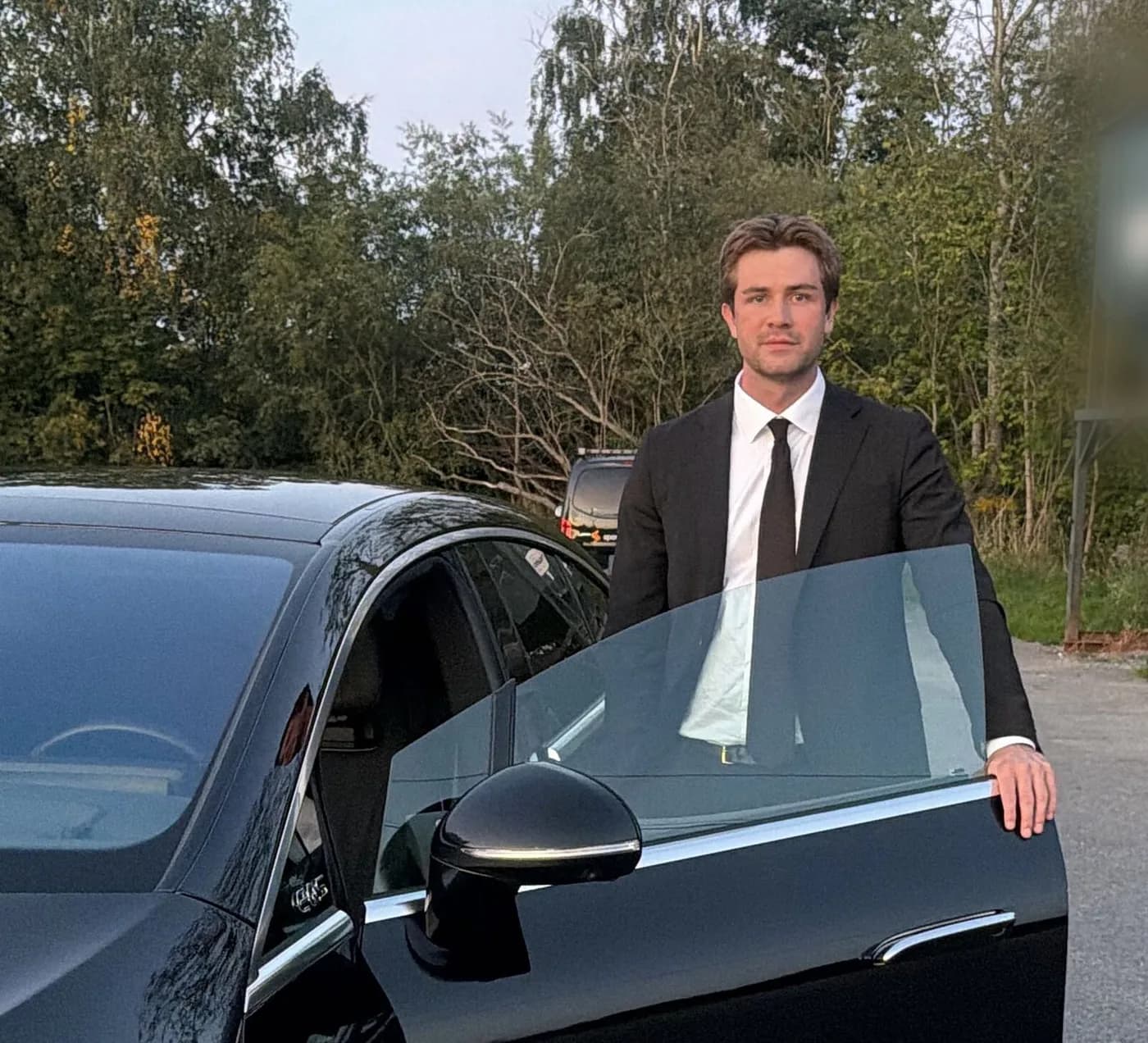 Christoffer Husby i dress ved en svart Mercedes, holder bakdøra åpen